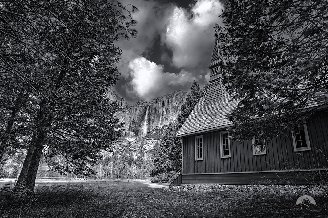 Elevate your space with the timeless beauty of Yosemite National Park through this stunning black and white landscape photo of the Yosemite Chapel, framed by the towering majesty of Upper Yosemite Falls. The absence of color enhances the dramatic contrast between the historic wooden chapel and the raw power of the cascading waterfall, emphasizing the intricate textures and striking interplay of light and shadow. This monochrome masterpiece captures the essence of Yosemite’s grandeur in a way that is both classic and captivating. Perfect for nature lovers and photography enthusiasts alike, this elegant print will bring a sense of serenity and adventure to any home or office. Add this breathtaking piece to your collection today!